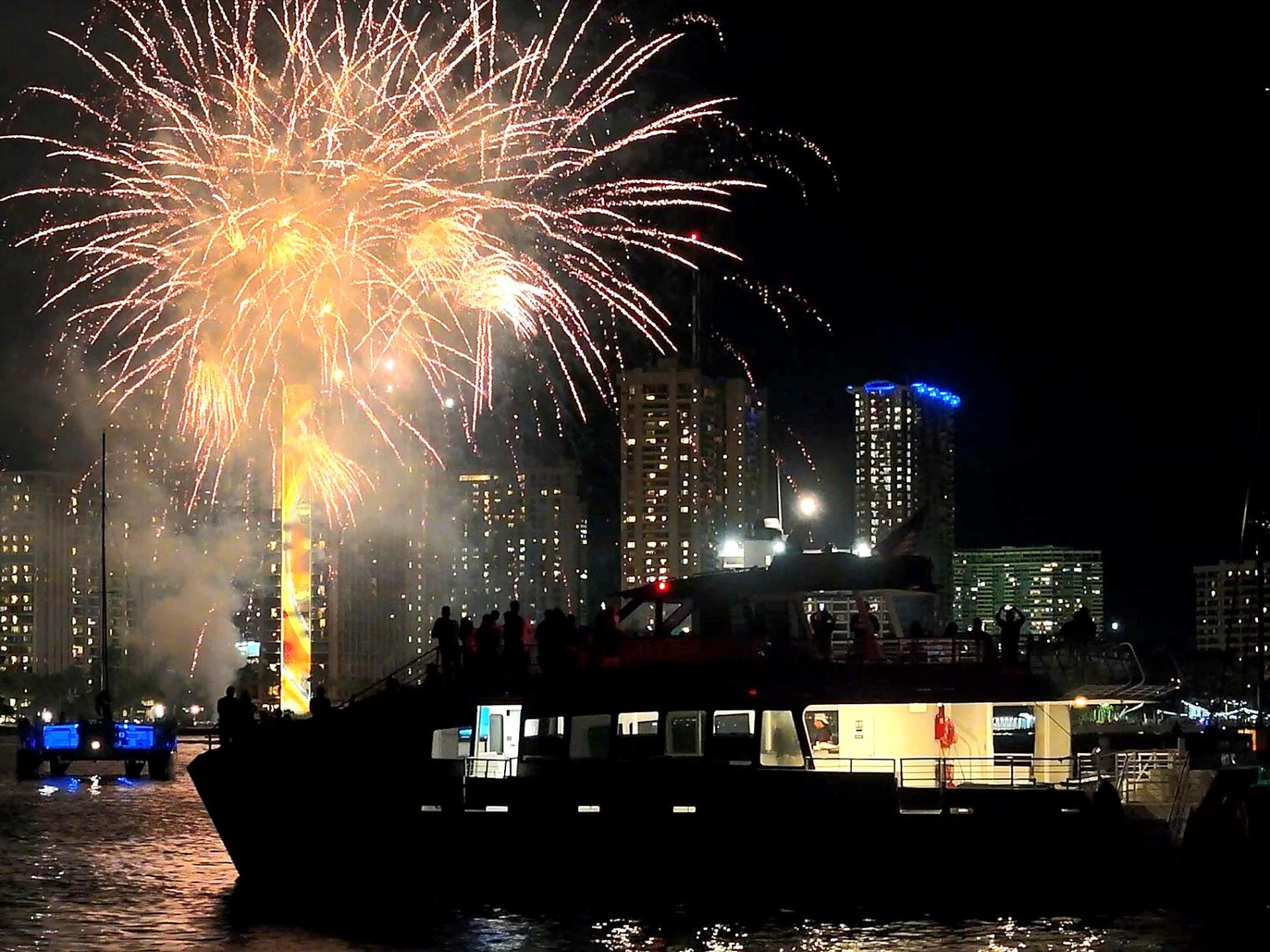 Nighttime fireworks display over a city skyline with a boat in the foreground.