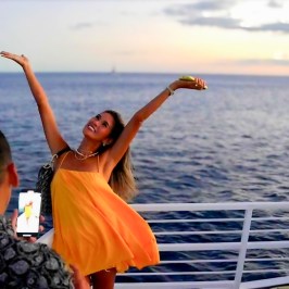 Woman poses happily on a boat at sunset, with a man photographing her.