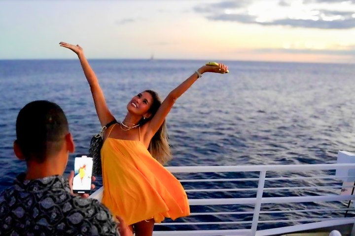 Woman poses happily on a boat at sunset, with a man photographing her.