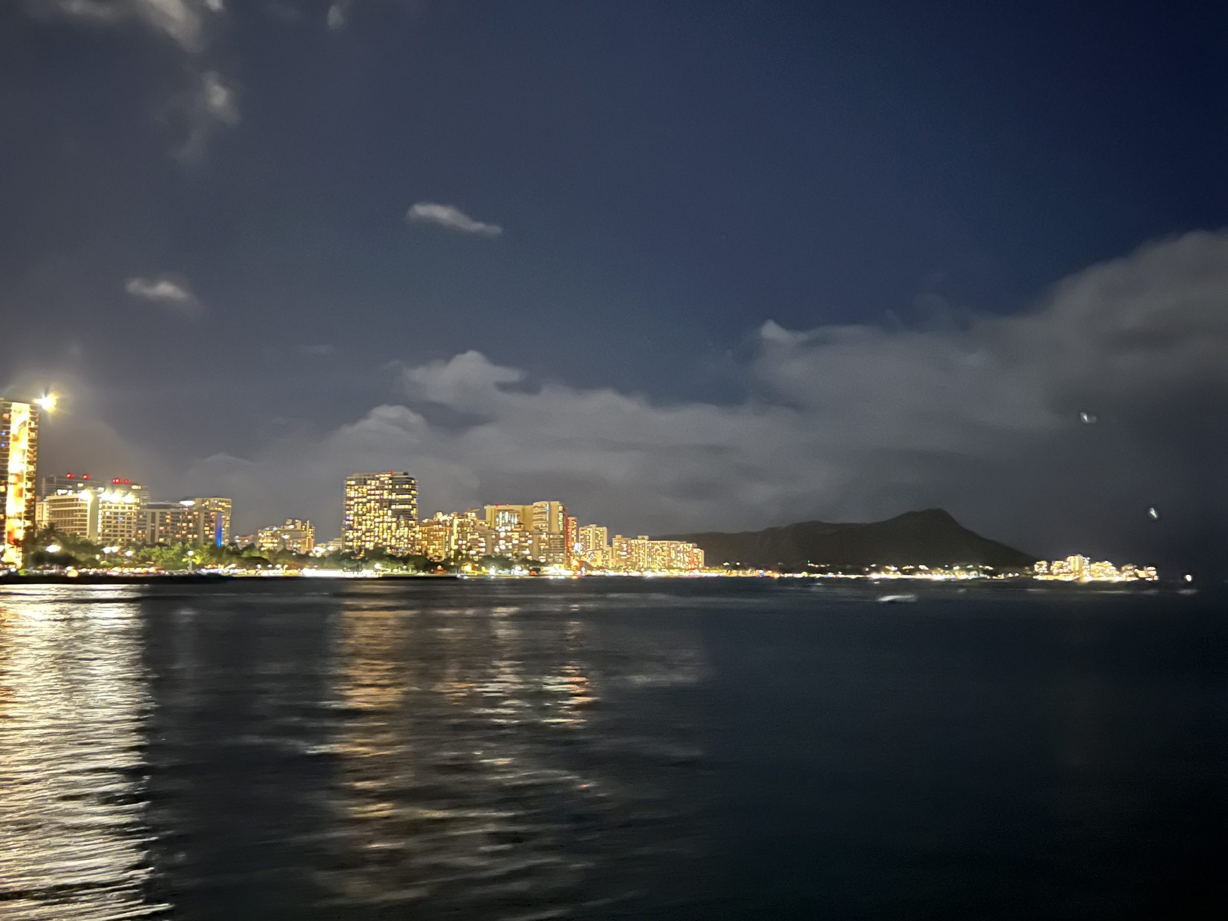 Night view of city skyline reflected on water with clouds in the sky.