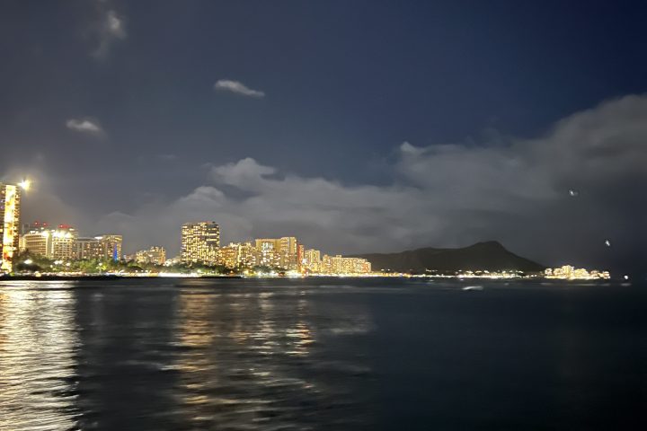 Night view of city skyline reflected on water with clouds in the sky.