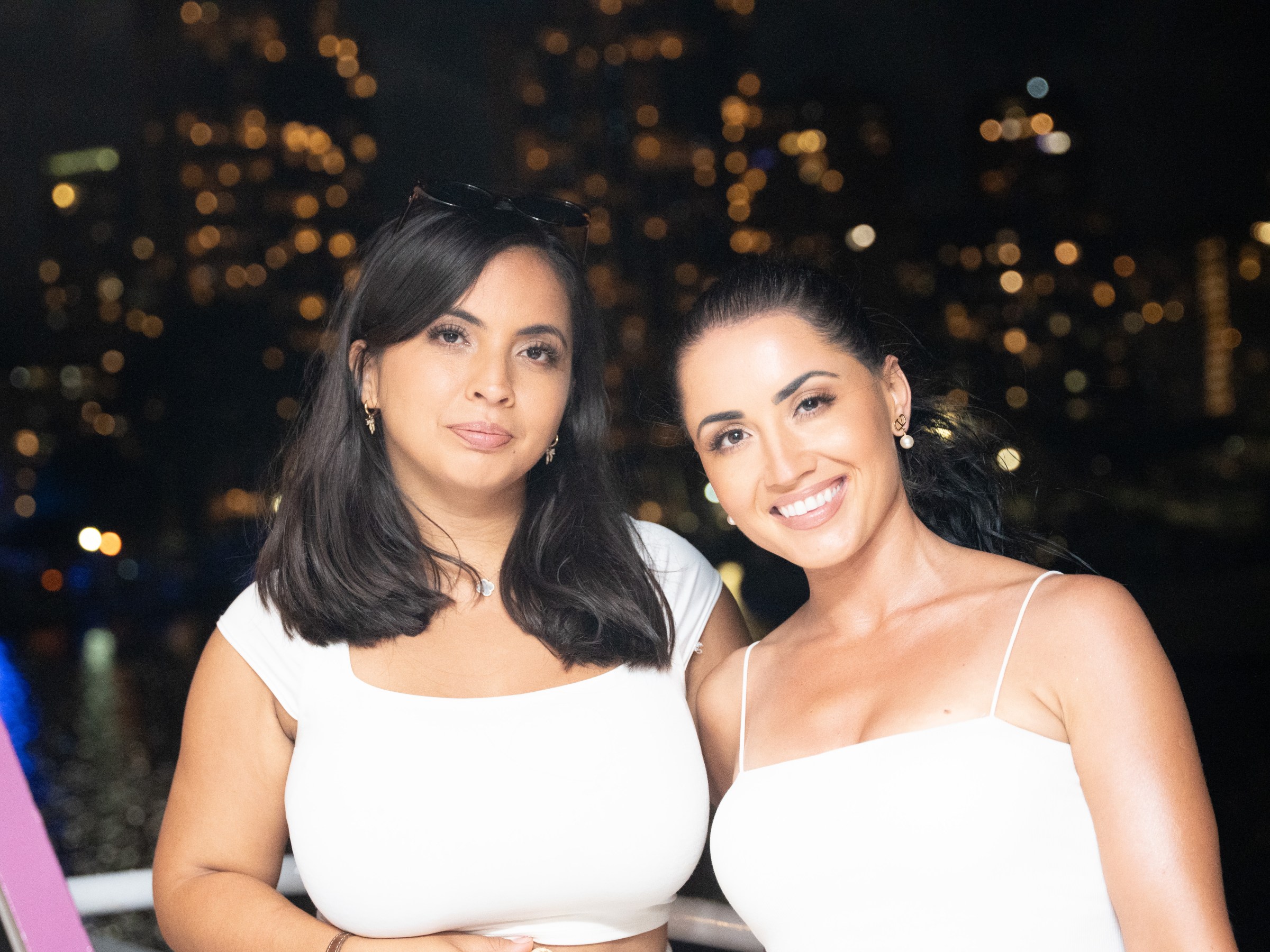 Two women in white tops smiling with a city nightscape in the background.