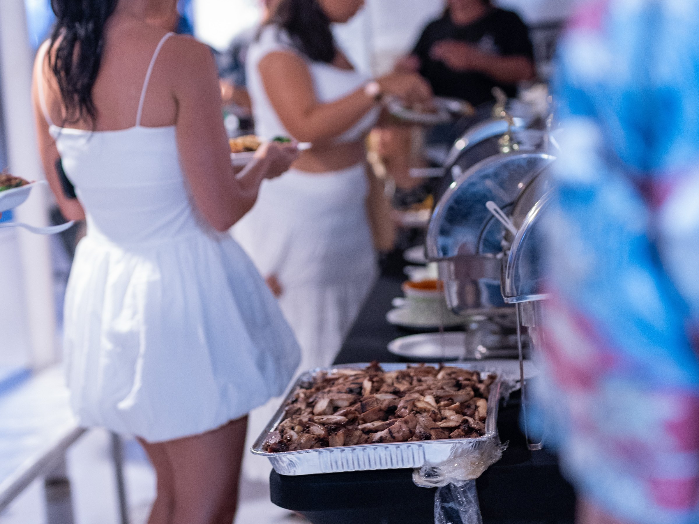 People in white outfits serving themselves from a buffet table indoors.