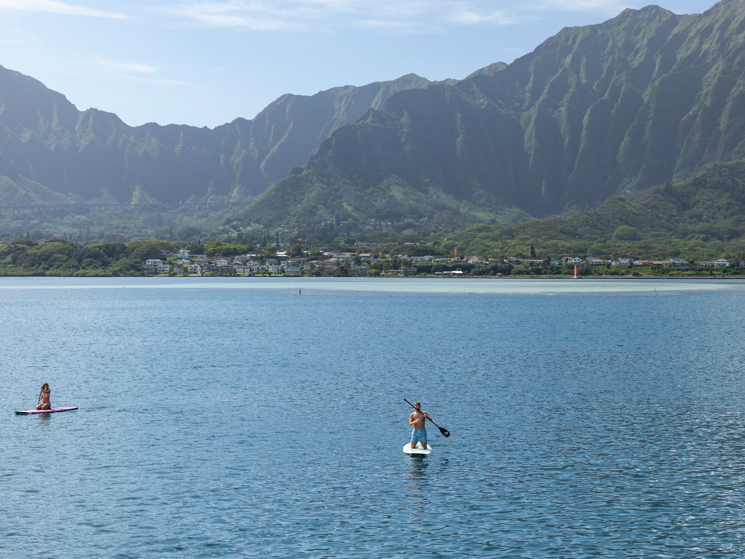 Two people paddleboarding on a lake with mountains and buildings in the background.