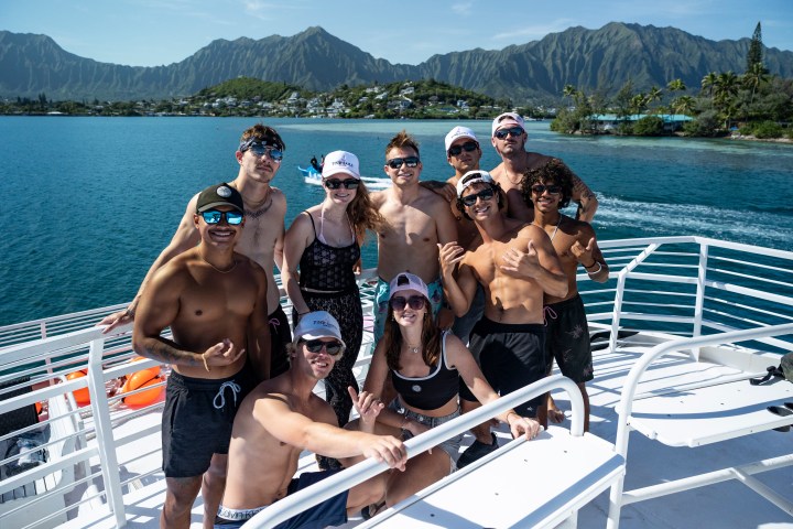 Group of people on a boat with mountains and ocean in the background.