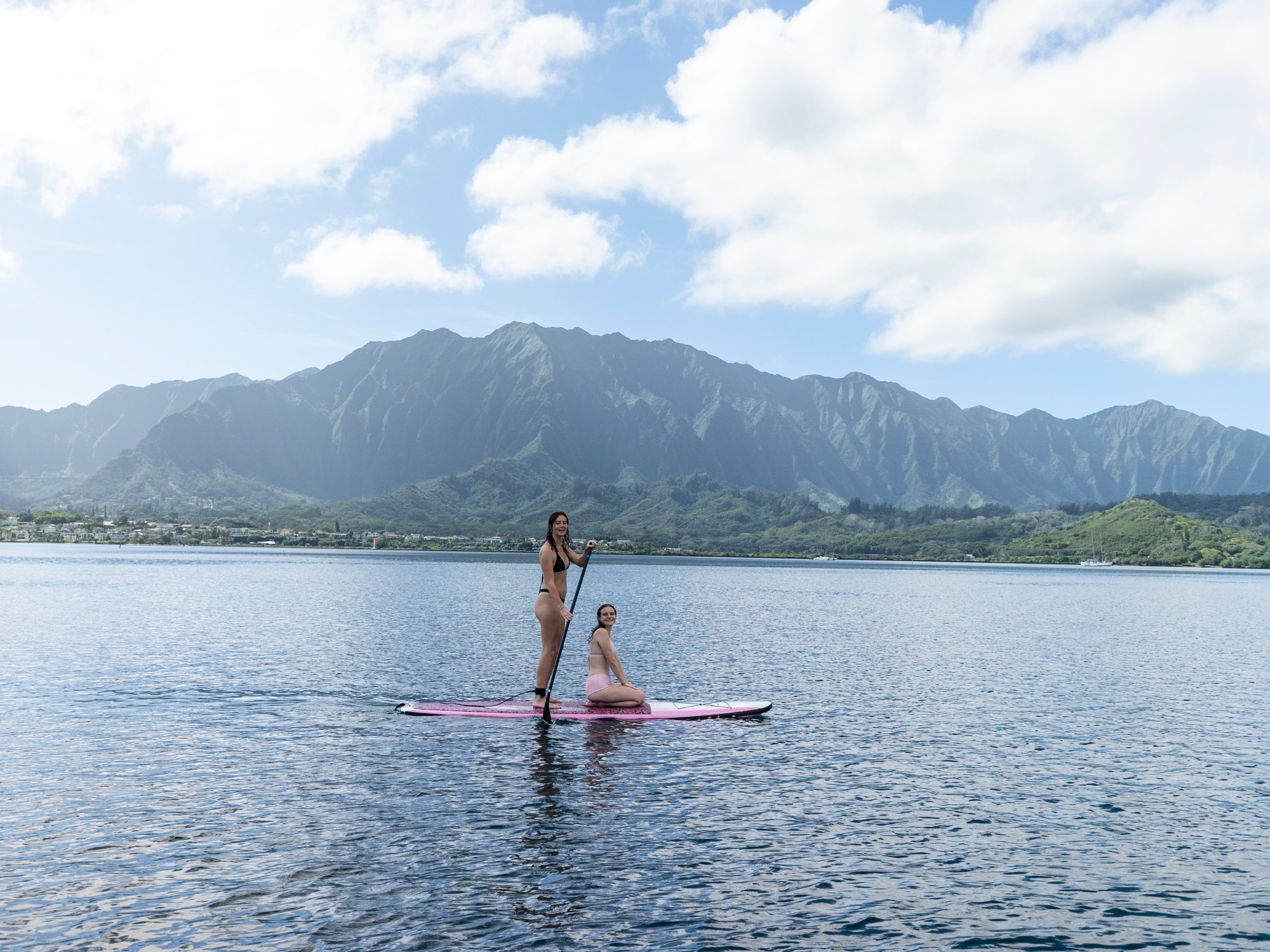 Two people on a paddleboard with mountains in the background and clear blue sky.