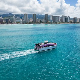 Boat on turquoise water with city skyline and mountains in the background.